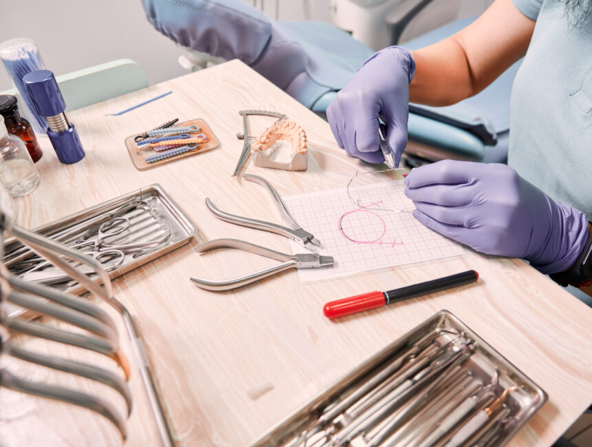 Close up view of female dentist in sterile gloves cutting braces wire while sitting at the table with orthodontic tools. Orthodontist preparing wire for braces attachment. Concept of dentistry.